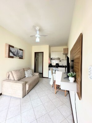 A living room with a sofa, a dining table with chairs, a ceiling fan, and a kitchen in the background. - Apartment in Taperapua with pool on Rua Arena Axe Moi (Porto Seguro)