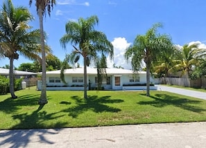 A single-story house with a white exterior, a front lawn, and palm trees. - Fantastic 4-bedroom house 1 block from ocean in charming Satellite Beach (Satellite Beach)