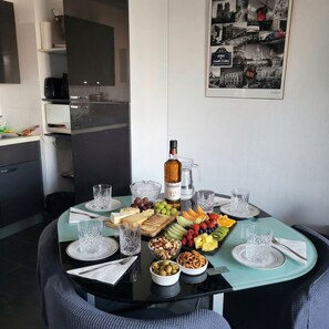 A dining table set with a bottle of wine, glasses, and a variety of snacks and fruits. - Spacious studio apartment with a view of the docks, a terrace, an elevator, and parking (Sète)