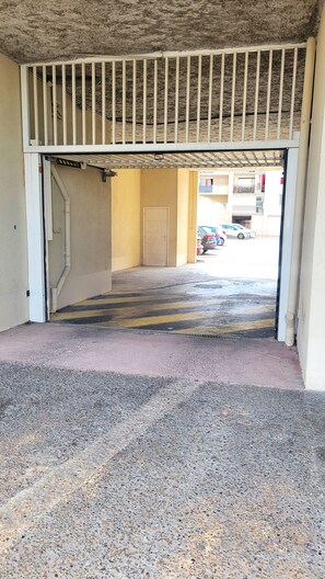 An entrance with a metal gate, a concrete floor, and a view of parked cars and buildings in the background. - Spacious studio apartment with a view of the docks, a terrace, an elevator, and parking (Sète)