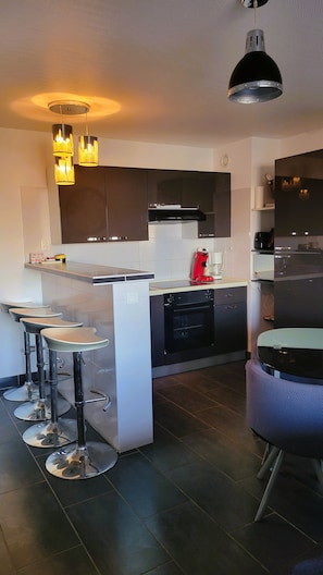 A modern kitchen with a central island, bar stools, a dishwasher, and a coffee machine. - Spacious studio apartment with a view of the docks, a terrace, an elevator, and parking (Sète)