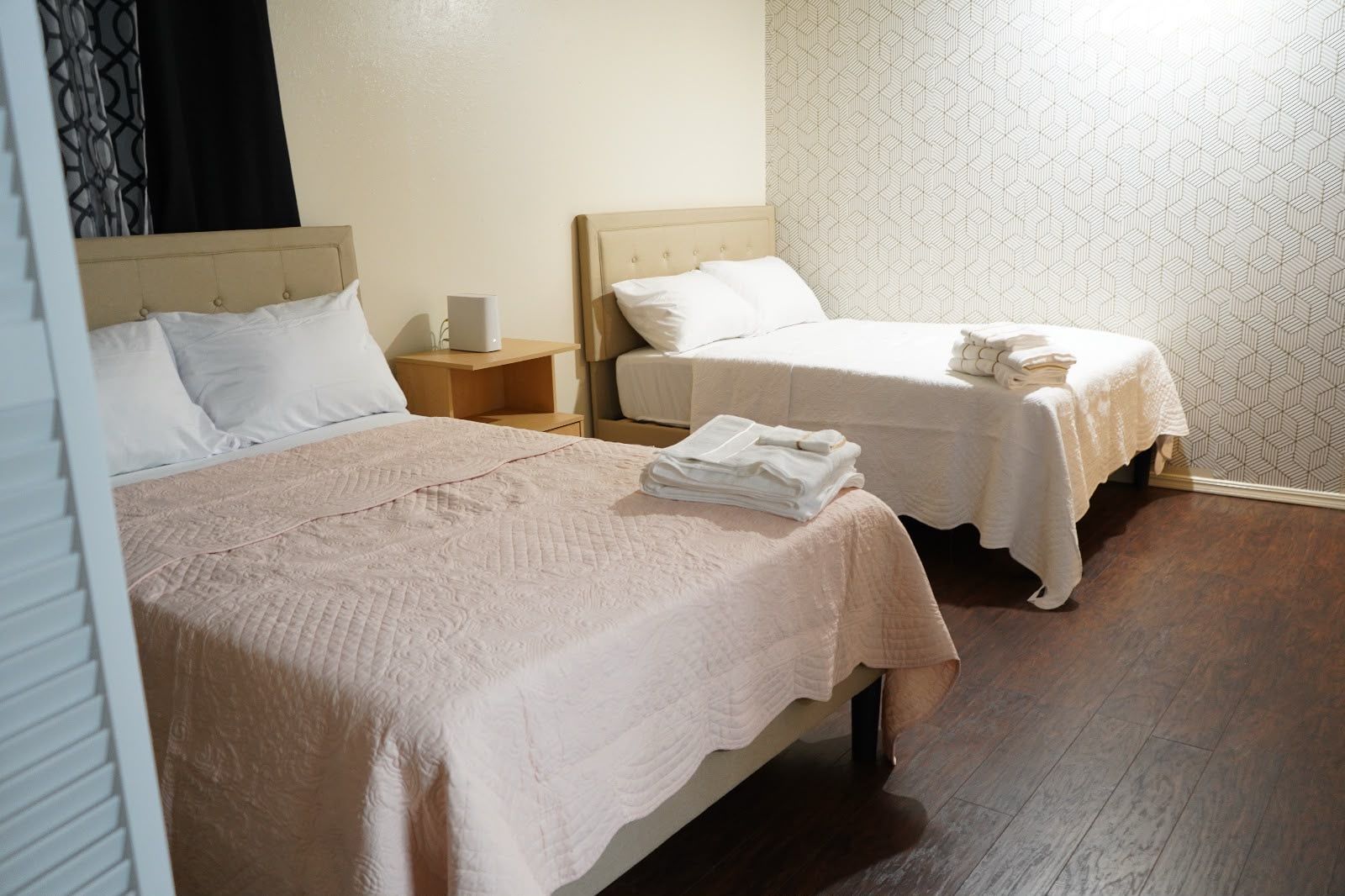 Une chambre d’hôtel avec deux lits, une table de chevet avec une lampe et un mur décoré d’un motif.