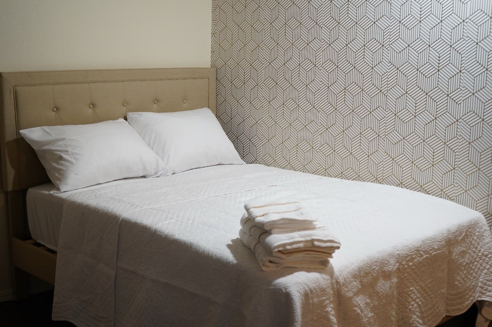 A neatly made bed with a headboard, white bedding, and a folded towel on the side.