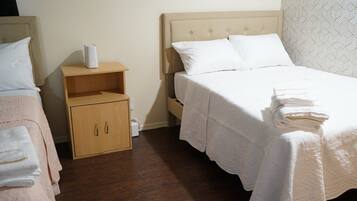 Habitación de hotel con dos camas, una mesita de noche de madera con un dispositivo blanco, un armario de madera y una pared con diseño.