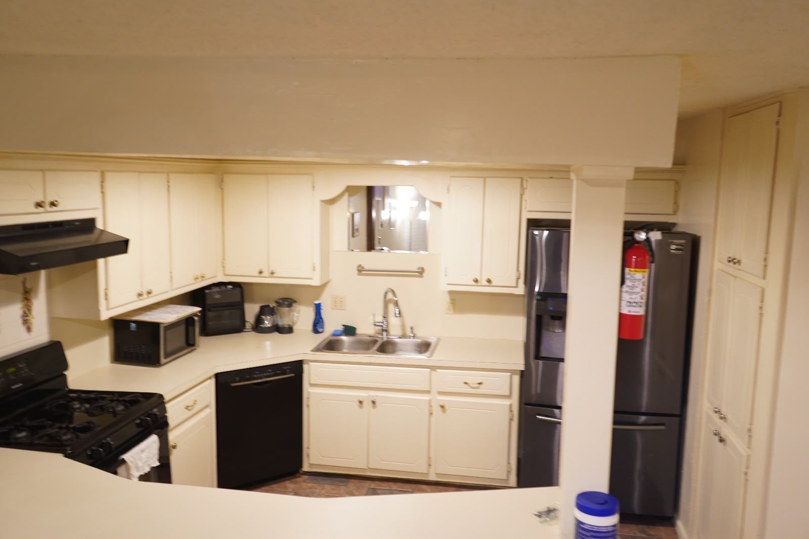 A compact kitchen with white cabinets, a stainless steel refrigerator, a dishwasher, and a microwave.