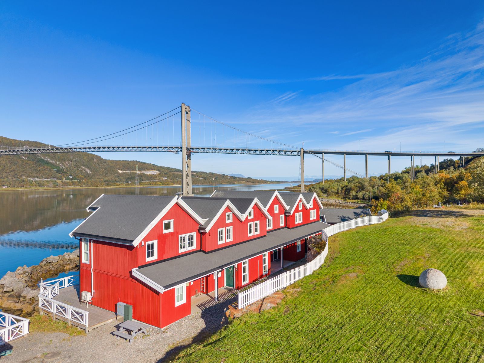 Un edificio rojo con un muelle, una valla blanca y un puente al fondo.