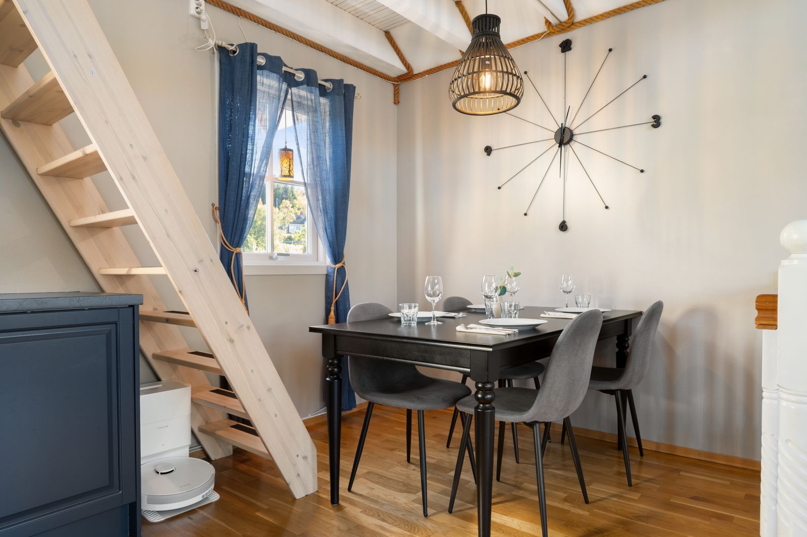 Een eetruimte met een tafel gedekt voor vier personen, een houten trap en een moderne lamp.