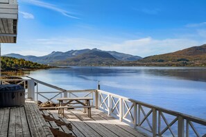 A wooden deck with a table and benches overlooking a calm lake with mountains in the background. - Tjeldsund rorbu by the sea (Tjeldsund)