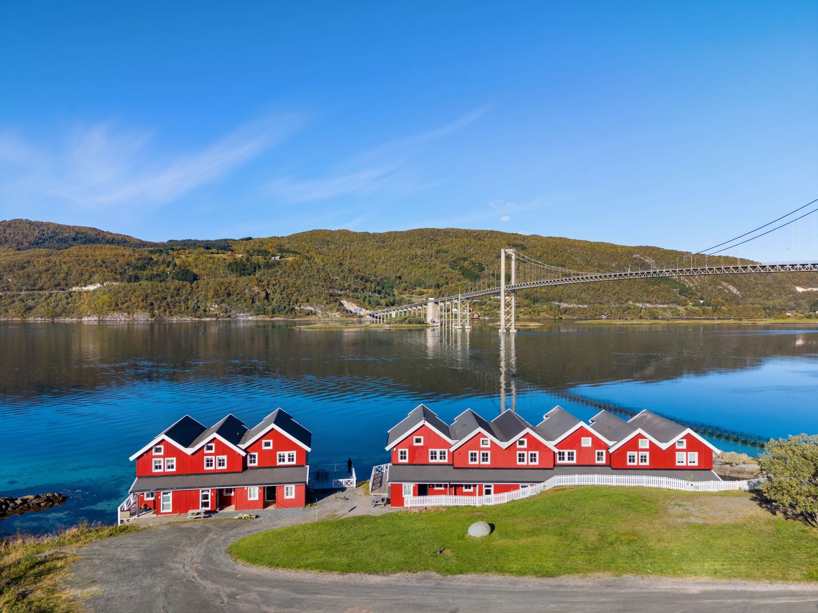 Une rangée de maisons rouges au bord d’un lac, avec un pont en arrière-plan.