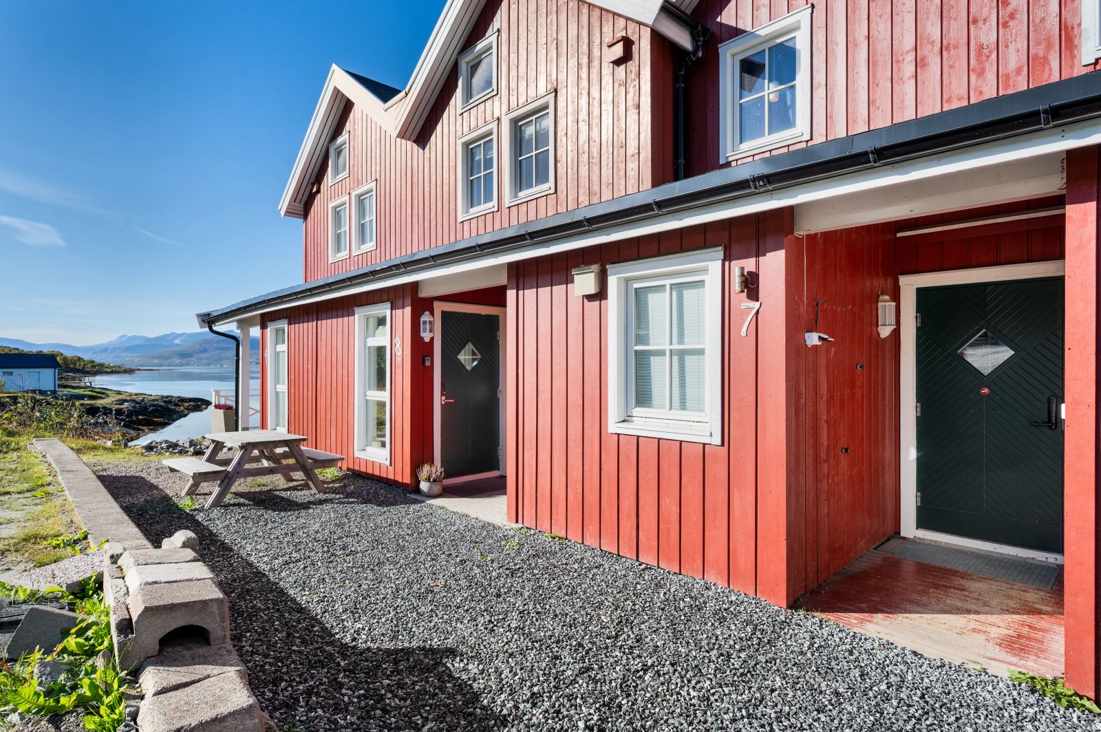 Een rode houten woning met een grindpad, een picknicktafel en uitzicht op het water.