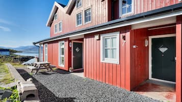 Een rode houten woning met een grindpad, een picknicktafel en uitzicht op het water.