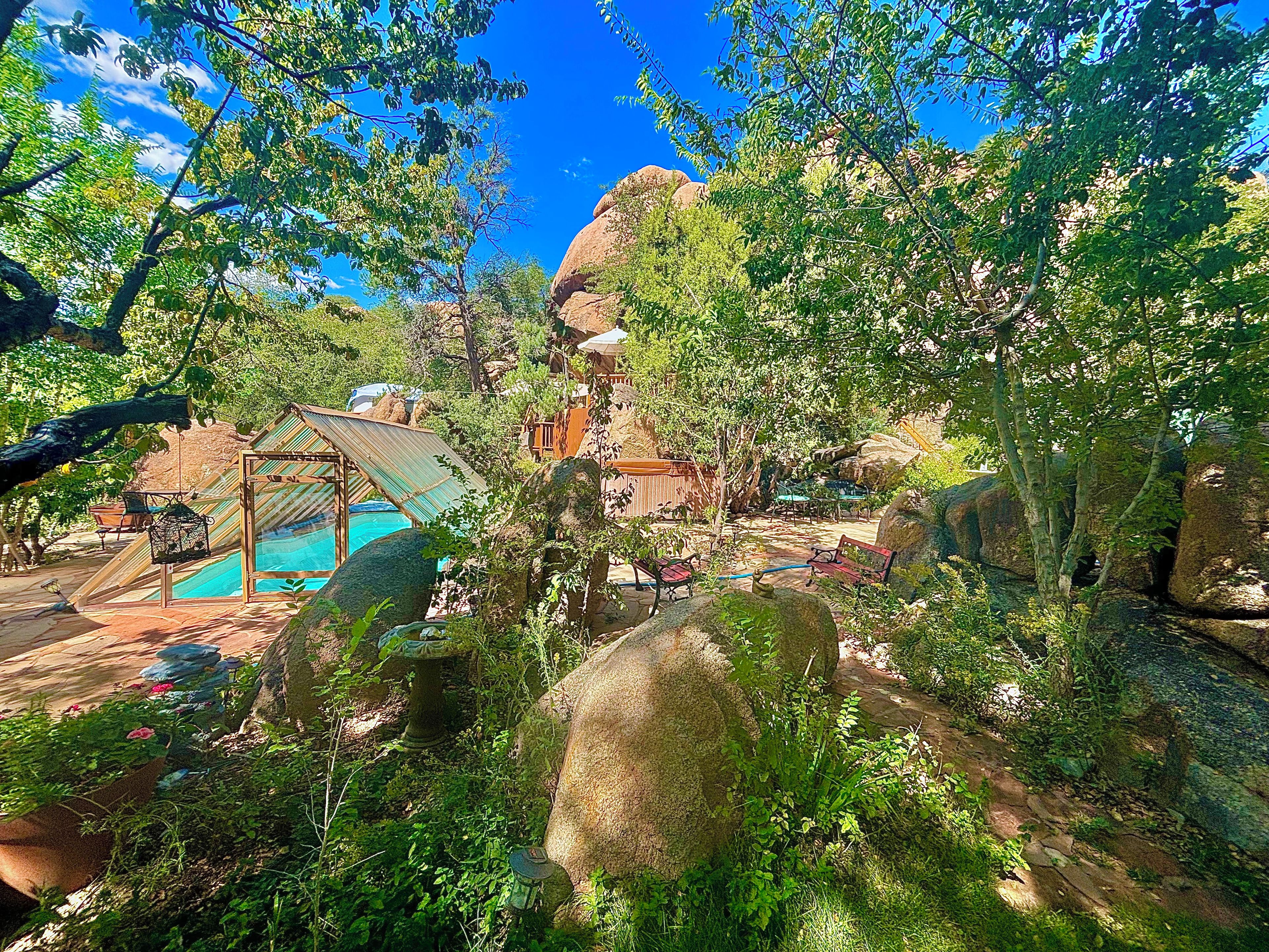 A pool area with a covered deck, surrounded by large rocks and greenery.