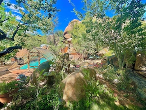 A pool area with a covered deck, surrounded by large rocks and greenery. - Heaven on Earth Retreat (Prescott)