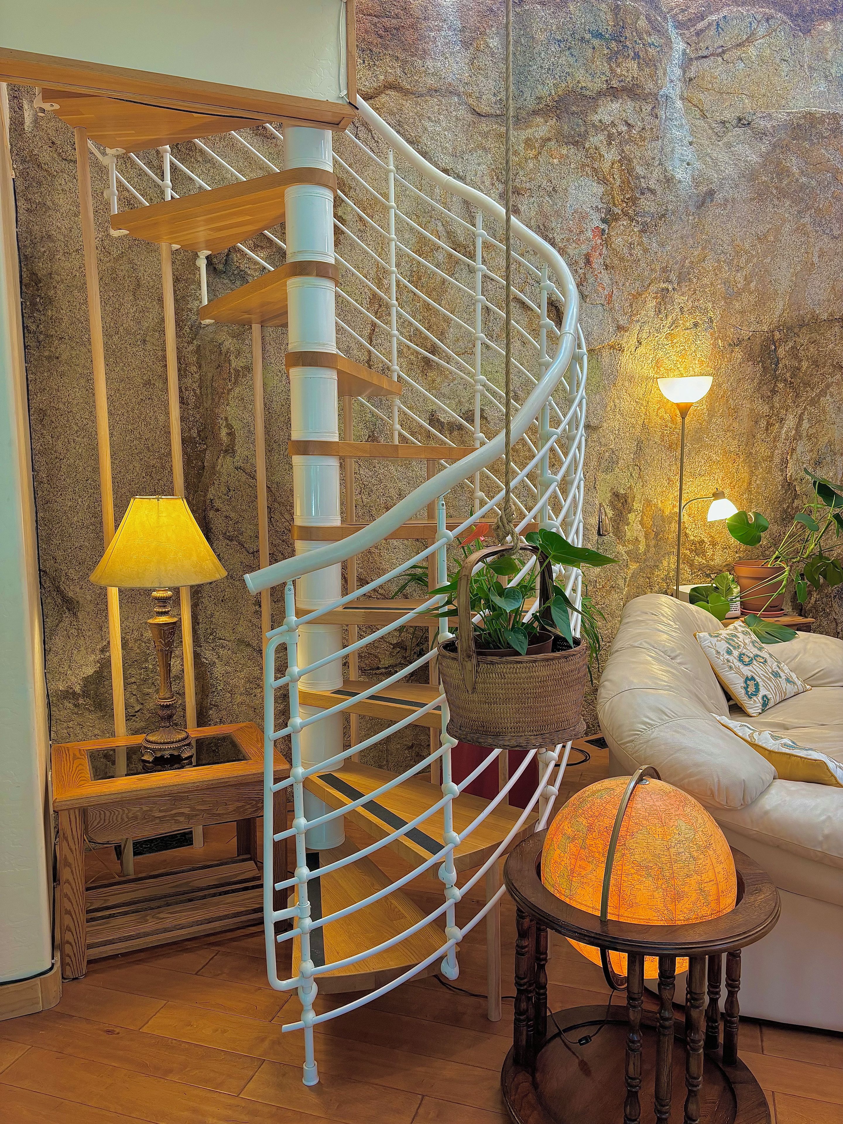 A spiral staircase with a white railing, a lamp, a globe, and a sofa with a plant.