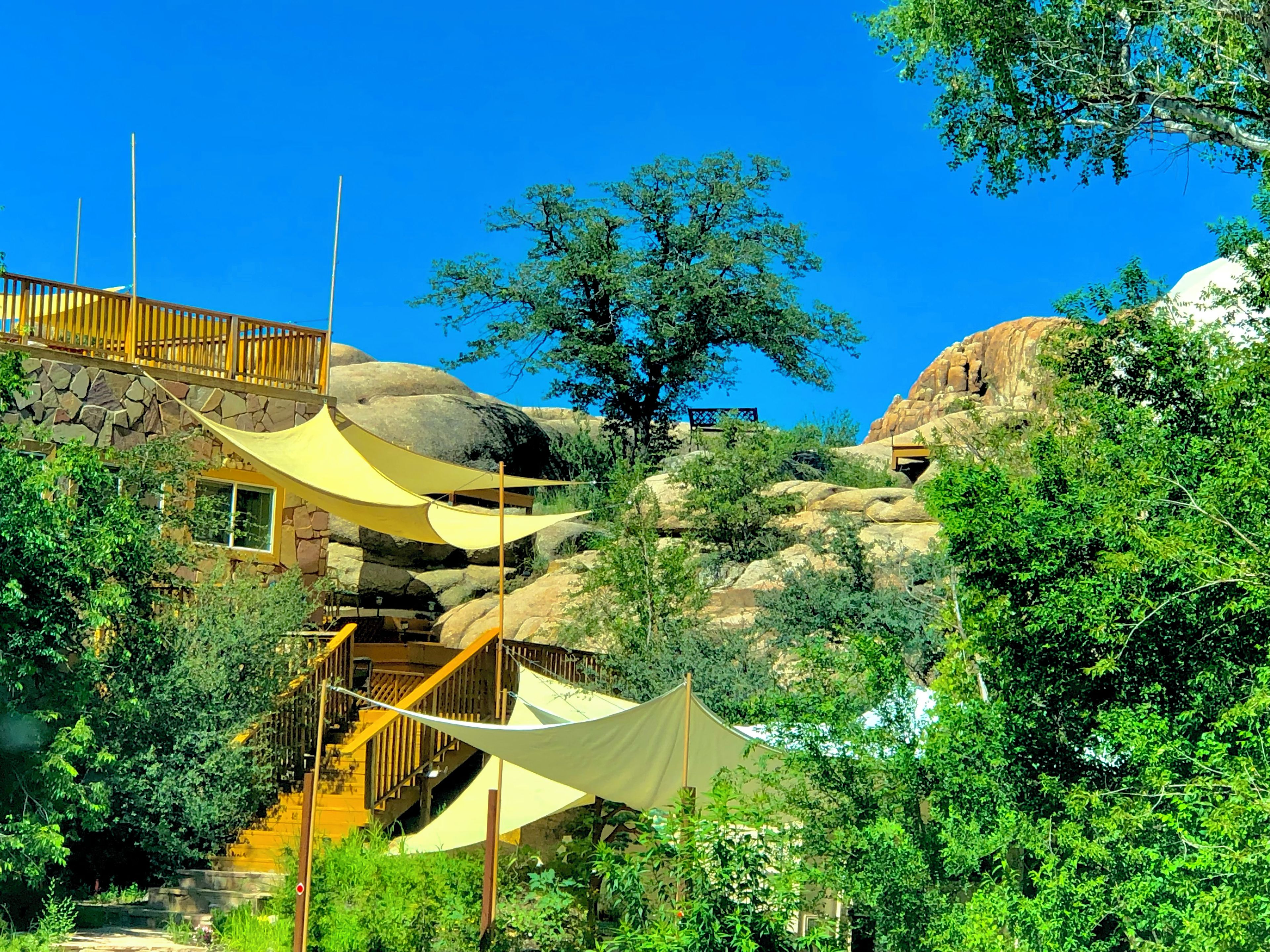 A building with a stone facade, wooden staircase, and a large tree in the background.