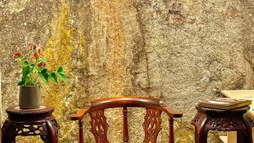 A wooden chair with a cushioned seat and backrest, positioned against a textured stone wall.