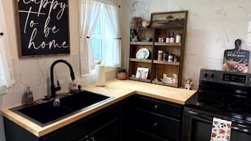 A kitchen with a black sink, wooden countertop, and black cabinets. There is a sign on the wall that says 'happy to be home.'