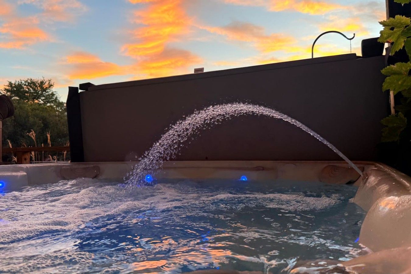 Ein Whirlpool mit Wasserspeier, umgeben von einer Holzterrasse und einem Sonnenuntergangshimmel.