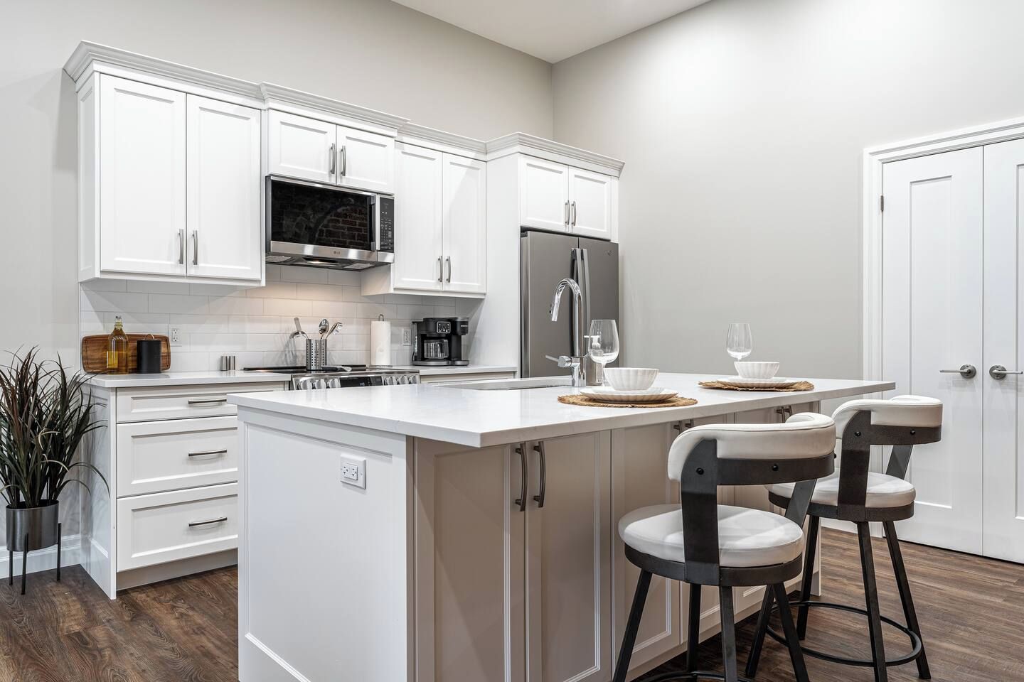A modern kitchen with white cabinetry, a stainless steel refrigerator, a built-in microwave, and a bar area with stools.