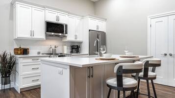 A modern kitchen with white cabinetry, a stainless steel refrigerator, a built-in microwave, and a bar area with stools.