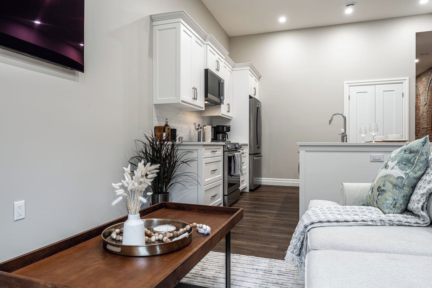 A modern kitchen with white cabinetry, a stainless steel refrigerator, and a dining area with a wooden table and a vase of dried flowers.