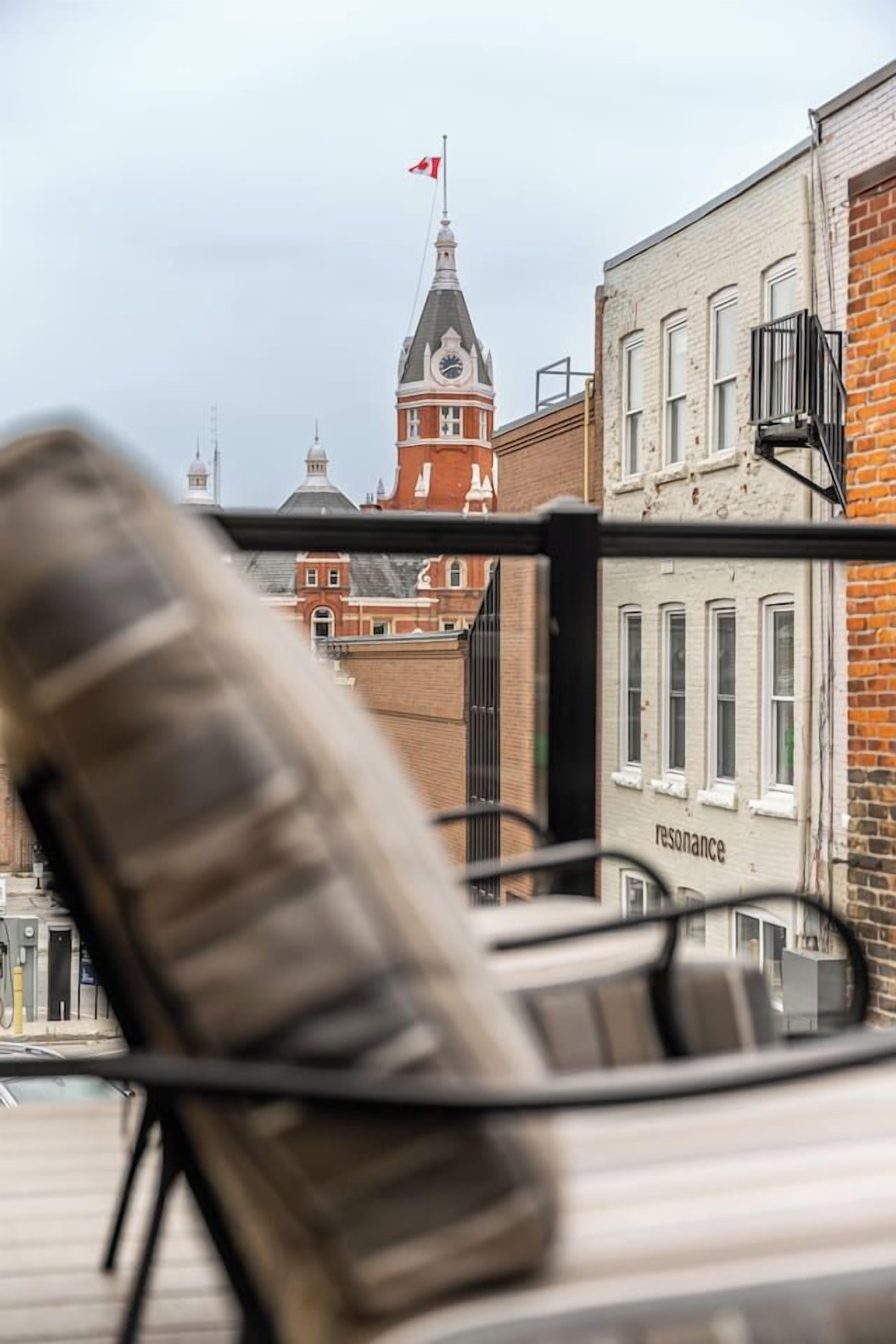 A chair with a metal frame and a cushion, positioned in front of a building with a clock tower and a red flag.