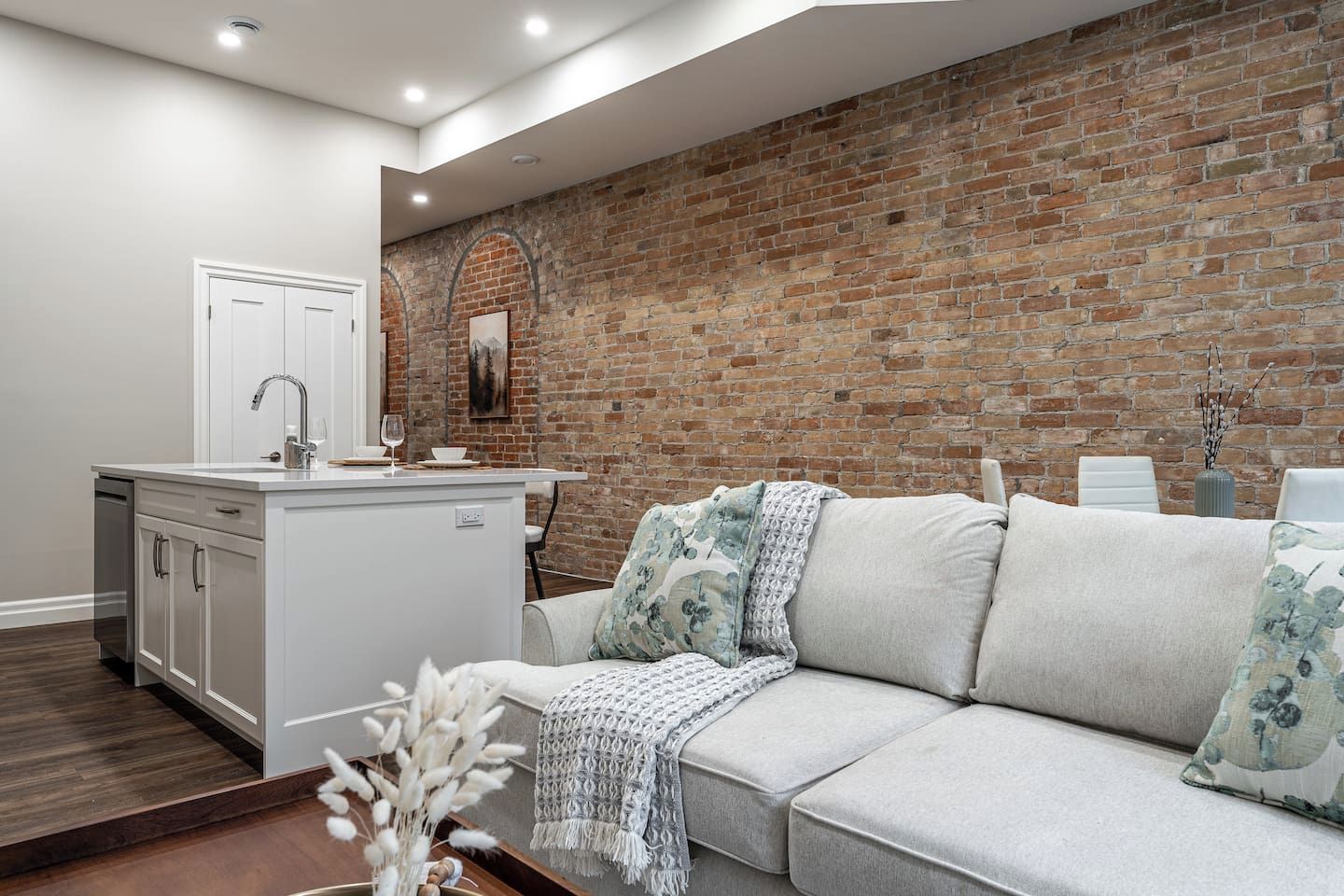 A modern living space with a kitchen island, a sofa with decorative pillows, and a brick wall.
