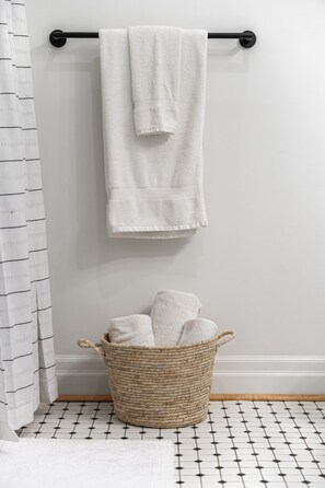 A bathroom with a white towel hanging on a black towel bar, a woven basket with towels, and a patterned floor. - Juno F5: The Curator’s Studio (Stratford)