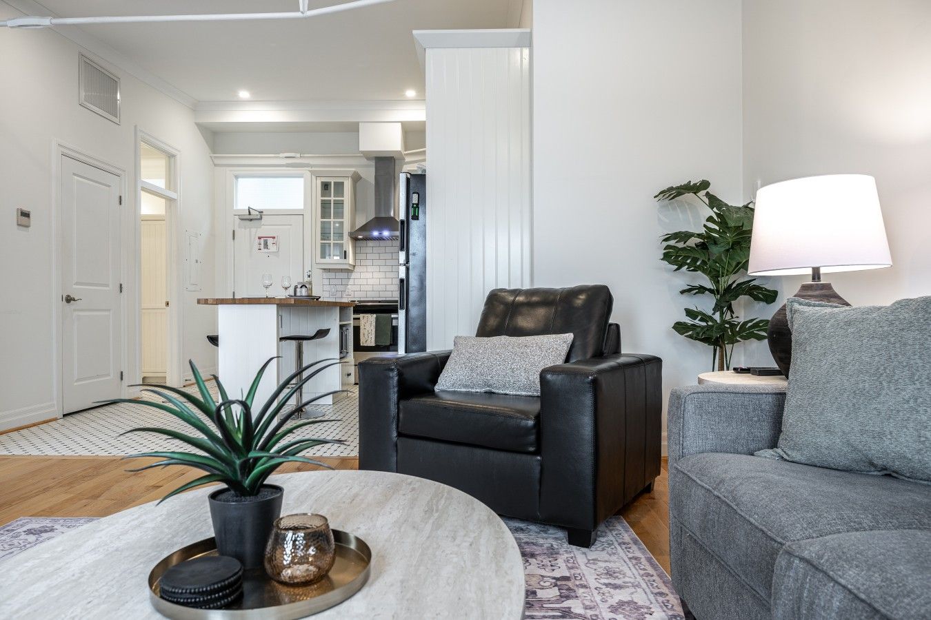 Un salon comprenant un fauteuil en cuir, un canapé gris, une table basse agrémentée d’objets décoratifs et une lampe.