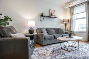 A modern living room with a leather sofa, grey armchair, and a round coffee table. - Juno F5: The Curator’s Studio (Stratford)