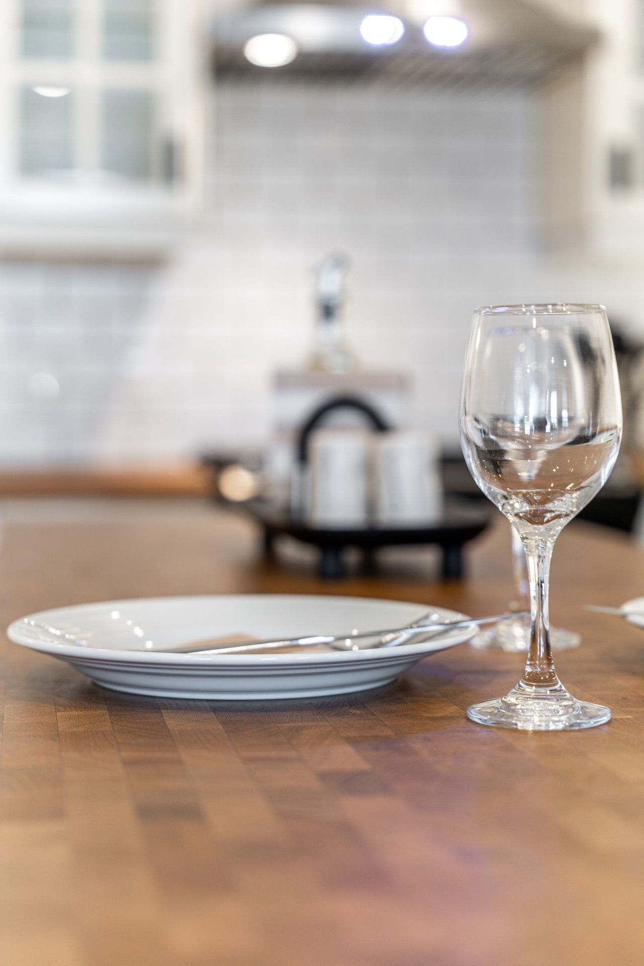 Une table à manger avec un verre à vin et des assiettes, un coin cuisine avec une cuisinière et des placards en arrière-plan.
