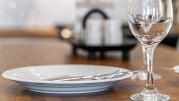Une table à manger avec un verre à vin et des assiettes, un coin cuisine avec une cuisinière et des placards en arrière-plan.