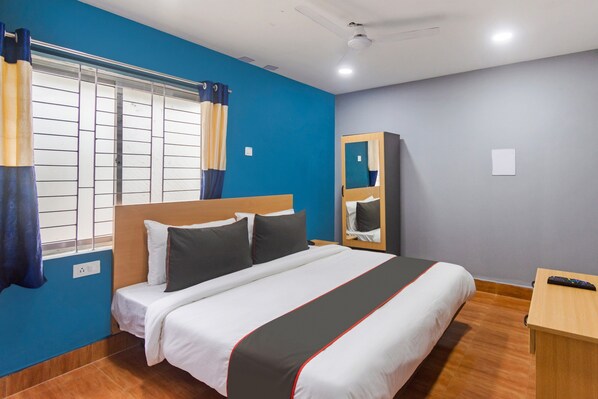 A hotel room with a bed, a wooden nightstand, a mirror, a window with curtains, and a ceiling fan.