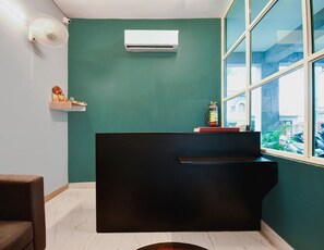 A room with teal walls, a black desk, a white air conditioner, a fire extinguisher, and a window with a view of the outside.