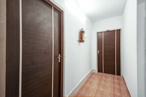 A hallway with two wooden doors, a fire extinguisher mounted on the wall, and a wooden floor.
