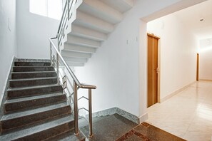 A staircase with metal railings leading to a landing, a wooden door, and a hallway with a tiled floor.