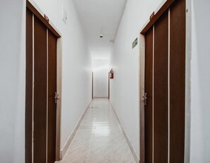 Un pasillo con puertas a ambos lados, un extintor en la pared y un letrero que indica la dirección de la salida.