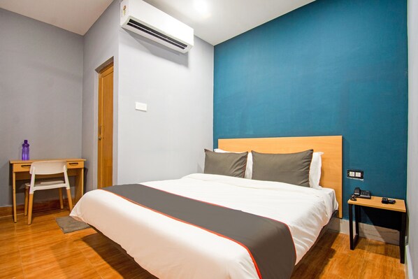 A hotel room with a bed, a desk, a chair, an air conditioner, and a nightstand.