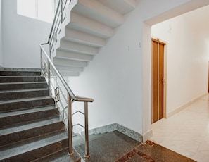 Una escala amb baranes metàl·liques que condueix a un badiu, una porta de fusta i un paviment de rajoles.