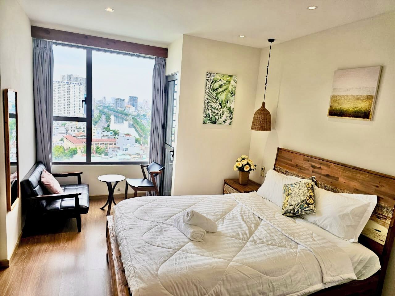 Une chambre d’hôtel dotée d’un grand lit, d’un coin salon avec un fauteuil et une petite table, d’une fenêtre donnant sur des bâtiments et d’œuvres d’art accrochées aux murs.