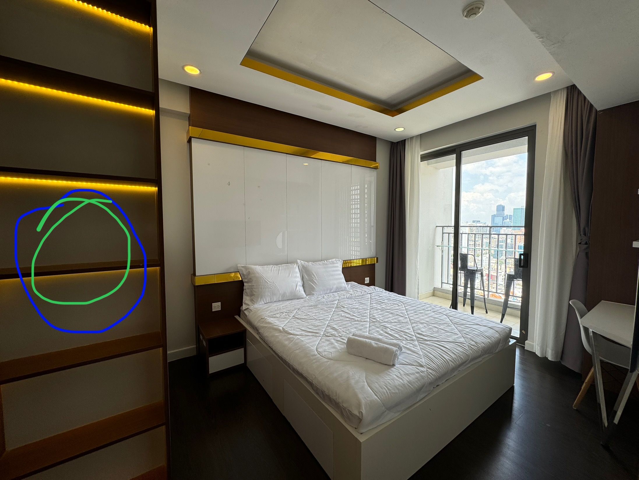 A hotel room with a bed, a wardrobe, a nightstand, a chair, and a balcony with a city view.