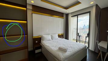 A hotel room with a bed, a wardrobe, a nightstand, a chair, and a balcony with a city view.