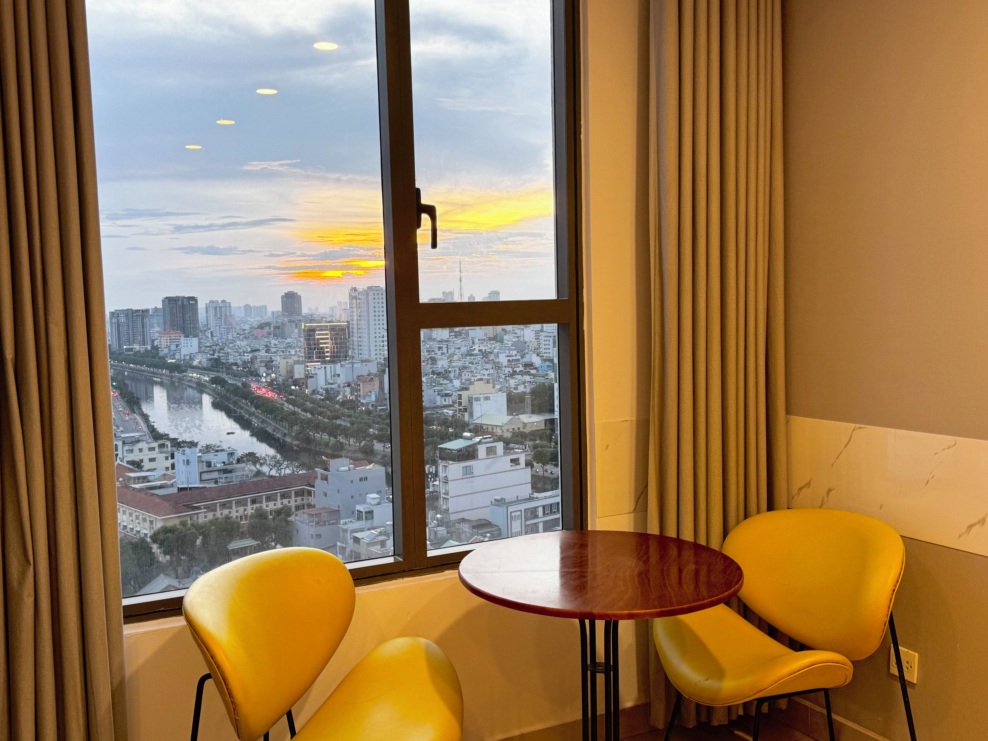 Una habitación con un ventanal grande, dos sillas amarillas y una mesa redonda pequeña.