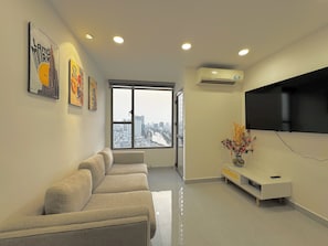 Una sala de estar moderna con un sofá, un televisor de pantalla plana montado en la pared y un ventanal con vistas a la ciudad.