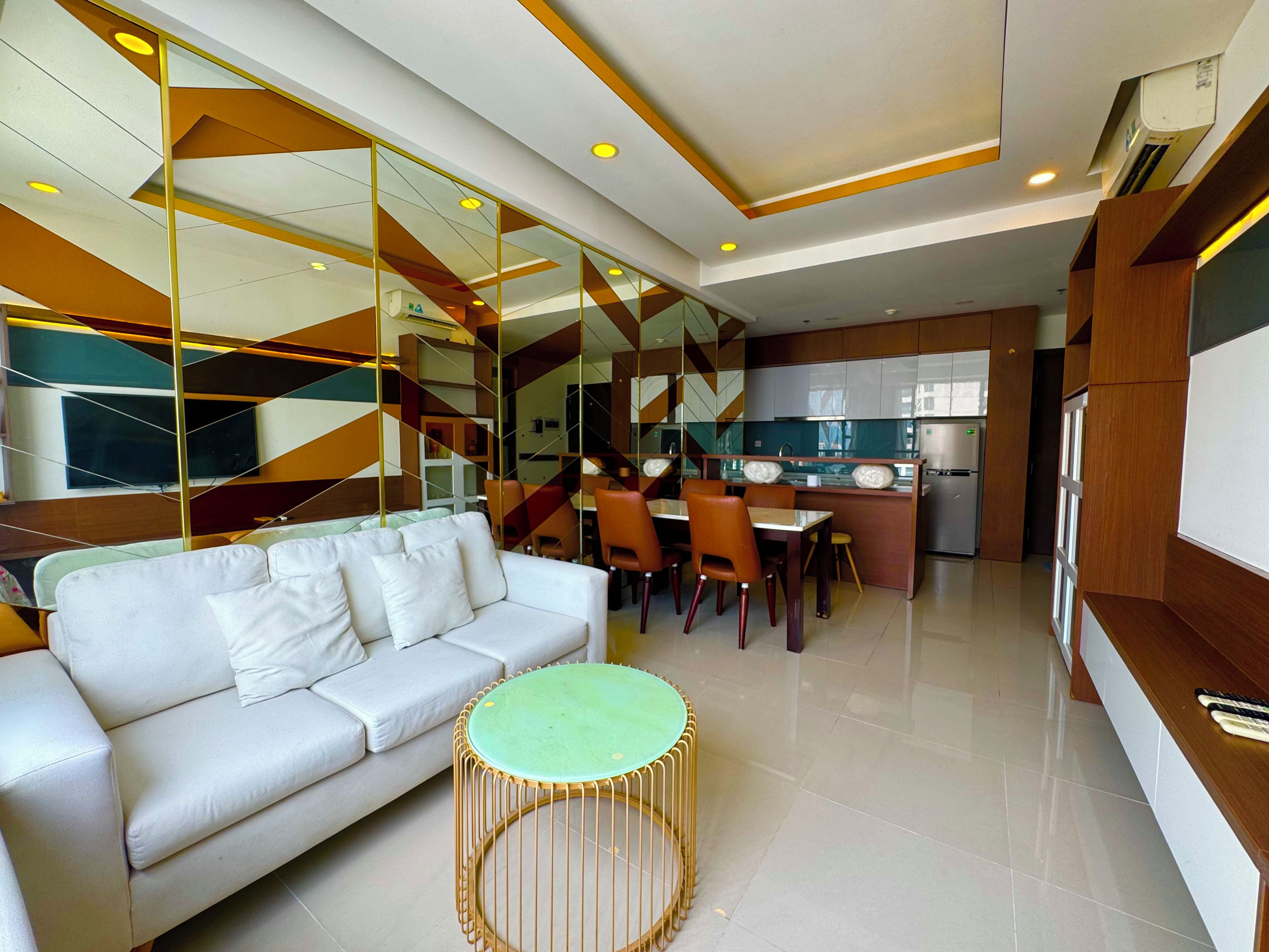 A modern living room with a sofa, a dining table with chairs, and a kitchen area in the background.