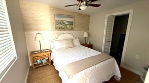 Separate bedroom with a comfortable queen bed, ceiling fan, nightstands and coastal artwork — your own quiet retreat. - Private 1BR Garden Cottage | 1 Mi to Madeira Beach (St. Petersburg)