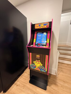 Una màquina recreativa de Pac-Man en una habitació amb un terra de fusta i una escala.
