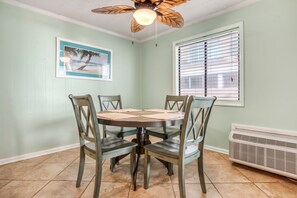 A dining area with a round table and four chairs, a ceiling fan, a window with blinds, and a wall-mounted air conditioner. - Calm Seasons by the Sea — 2BR Oceanview at Chateau by the Sea, North Myrtle Beach (North Myrtle Beach)