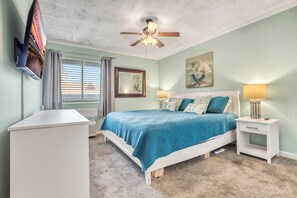 A bedroom with a bed, bedside tables, a ceiling fan, and a window with blinds. - Calm Seasons by the Sea — 2BR Oceanview at Chateau by the Sea, North Myrtle Beach (North Myrtle Beach)