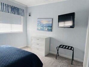 Ein Schlafzimmer mit einem Bett, einem Schminktisch, einer Bank, einem Gemälde und einem Fernseher.